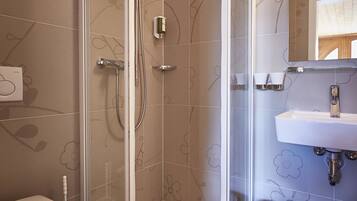 A modern bathroom with a glass-enclosed shower, a toilet, a sink, and a trash can.