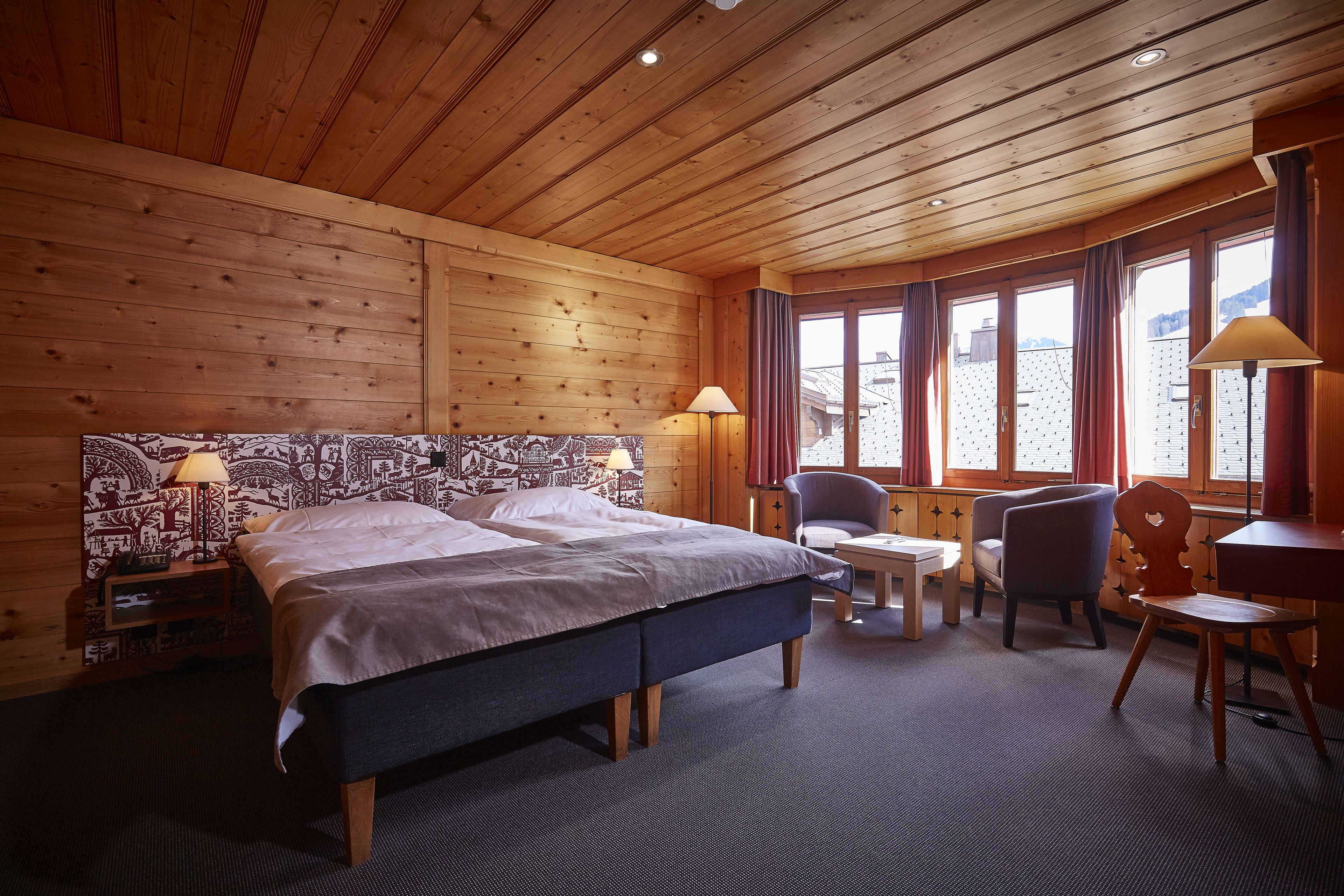 A wooden-paneled room with a bed, two chairs, a table, and a desk.