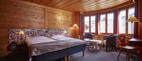 A wooden-paneled room with a bed, two chairs, a table, and a desk.