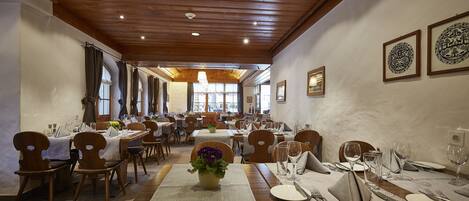 A restaurant with wooden ceiling beams, tables set with white tablecloths, and framed artwork on the walls.