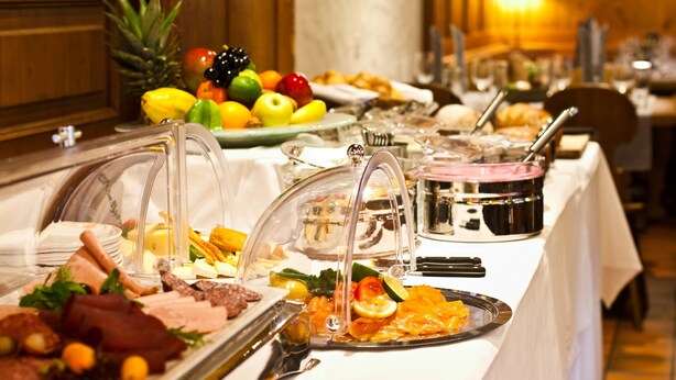 Un buffet proposant une variété de plats, notamment des fruits, des viandes et des fromages, disposés sur une table recouverte d’une nappe blanche.