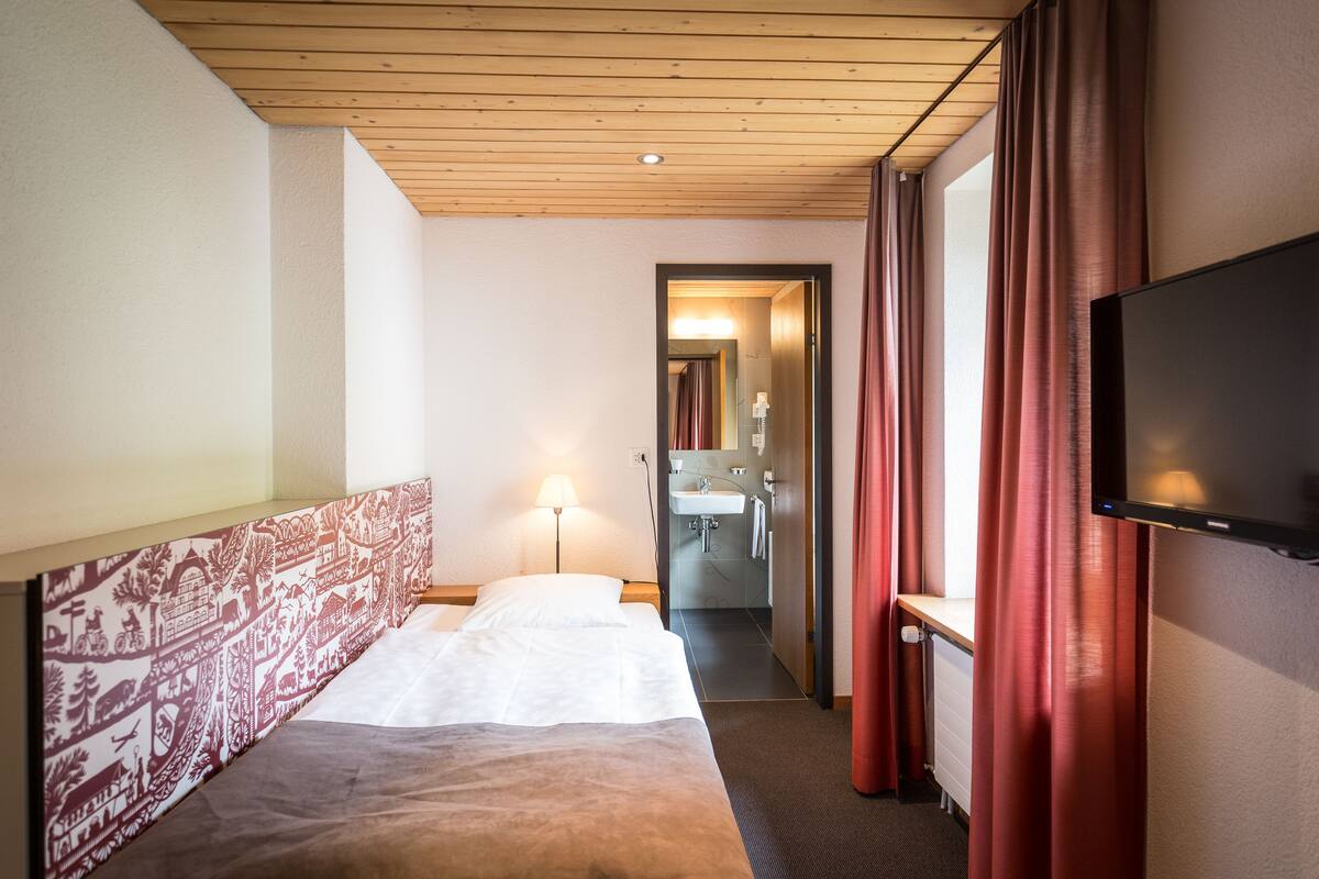 Habitación de hotel con cama, televisión, baño y techo de madera.