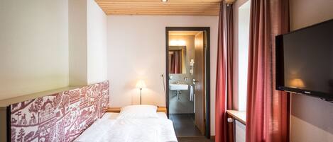 A hotel room with a bed, a TV, a bathroom, and a wooden ceiling.