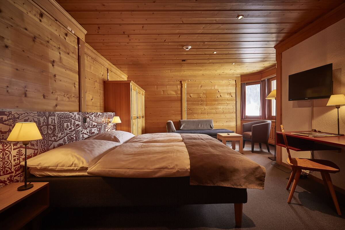 Un dormitorio de estilo cabaña de madera con cama, lámparas de noche, escritorio y televisión.