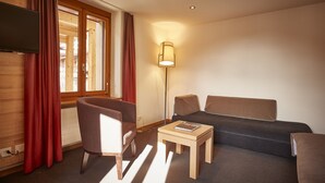 Une chambre d’hôtel équipée d’un canapé, d’un fauteuil, d’une petite table, d’une lampe et d’un téléviseur fixé au mur.