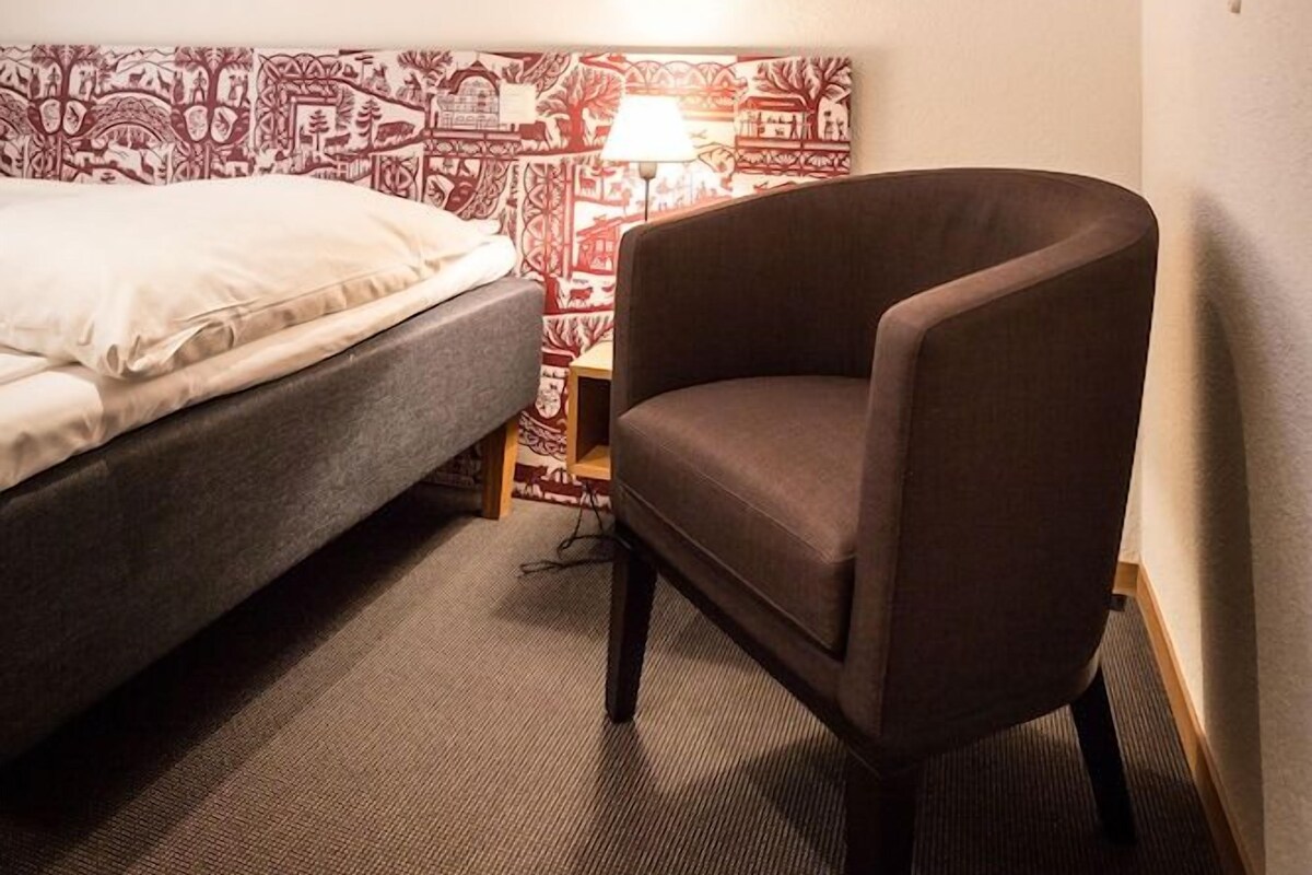 A hotel room with a bed, a chair, a lamp, and a patterned wall.