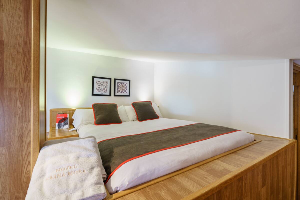 A neatly made bed with a white and grey blanket, a wooden headboard, and two framed pictures on the wall.