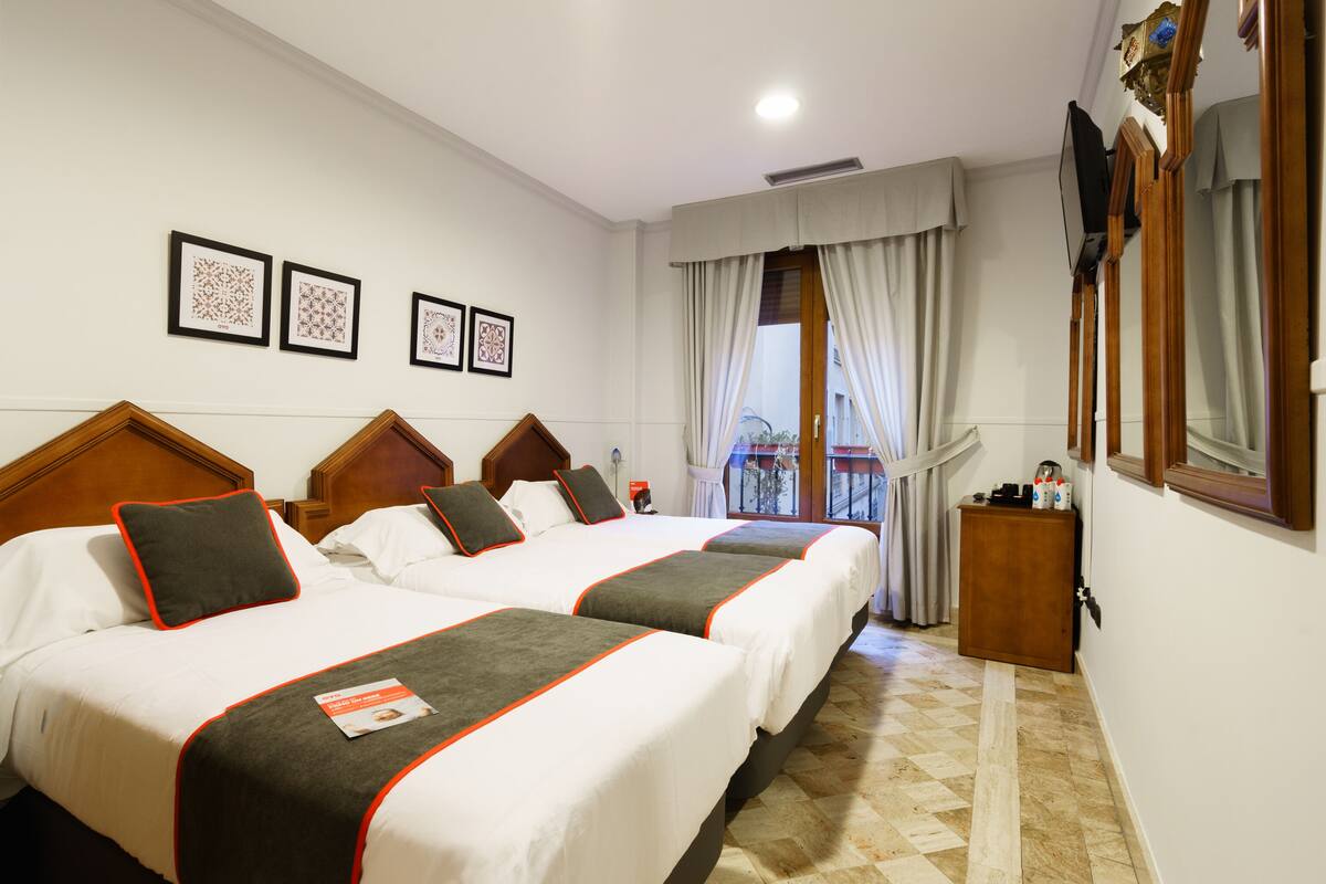 A hotel room with two beds, a wooden headboard, a window with curtains, and framed pictures on the wall.