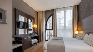 A hotel room with a large bed, a desk with a chair, a television, and a window with curtains.
