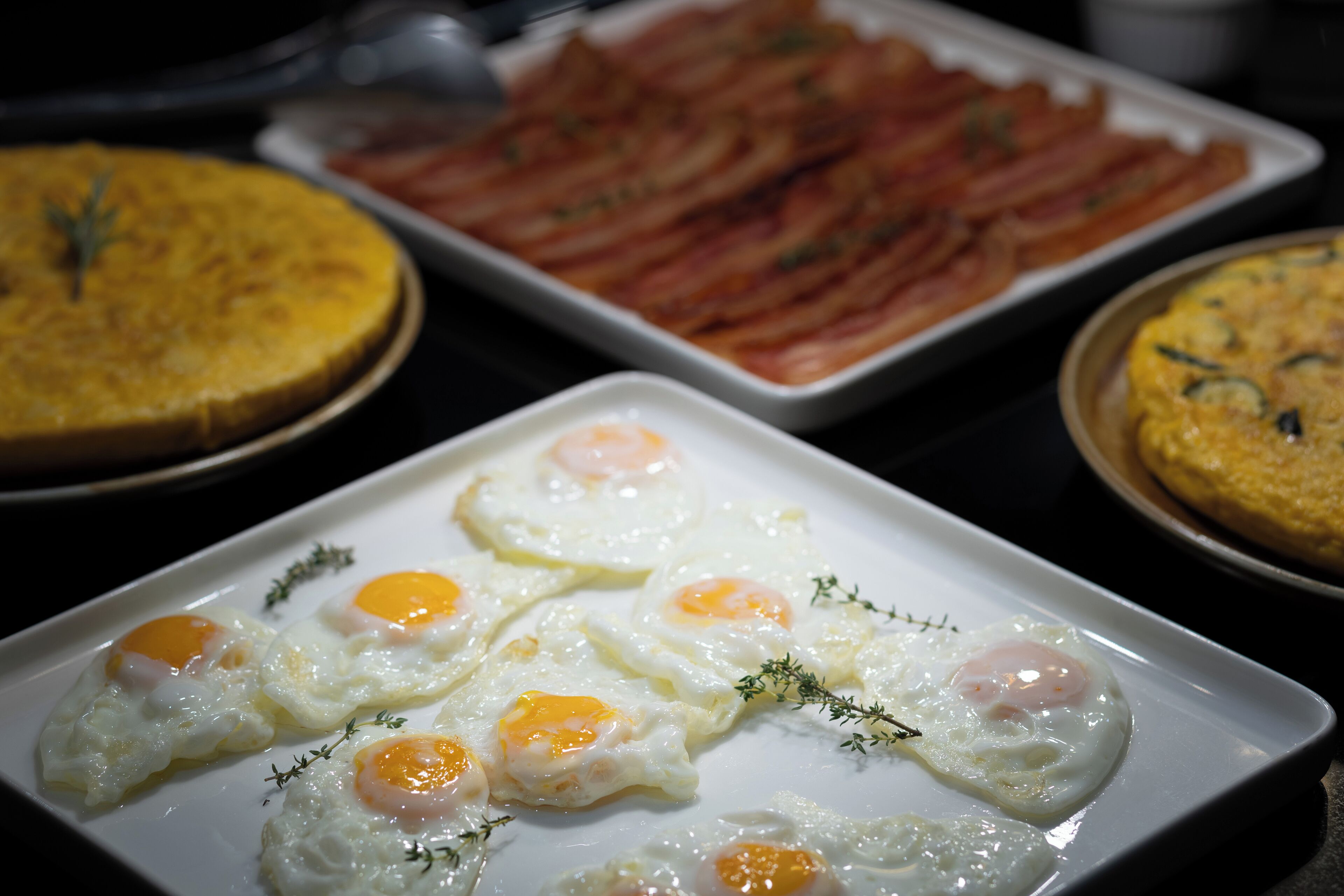 A breakfast buffet with various dishes including eggs, bacon, and a quiche.