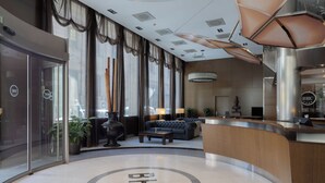 A modern hotel lobby with a reception desk, seating area, and large windows with curtains.