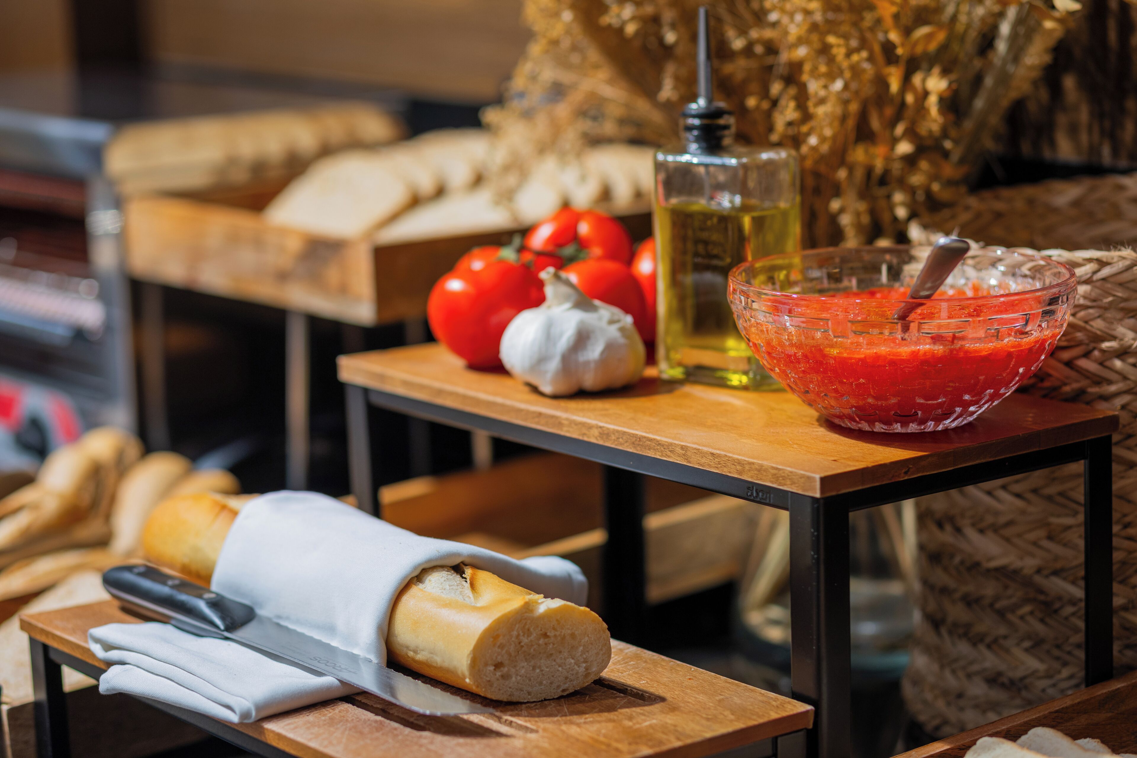A table with bread, tomatoes, garlic, and a bowl of red sauce.