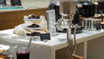 A coffee machine with a metal spout and a wooden handle, a glass display case with layered desserts, and a sign indicating a chocolate dessert.