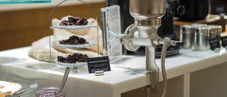 A coffee machine with a metal spout and a wooden handle, a glass display case with layered desserts, and a sign indicating a chocolate dessert.