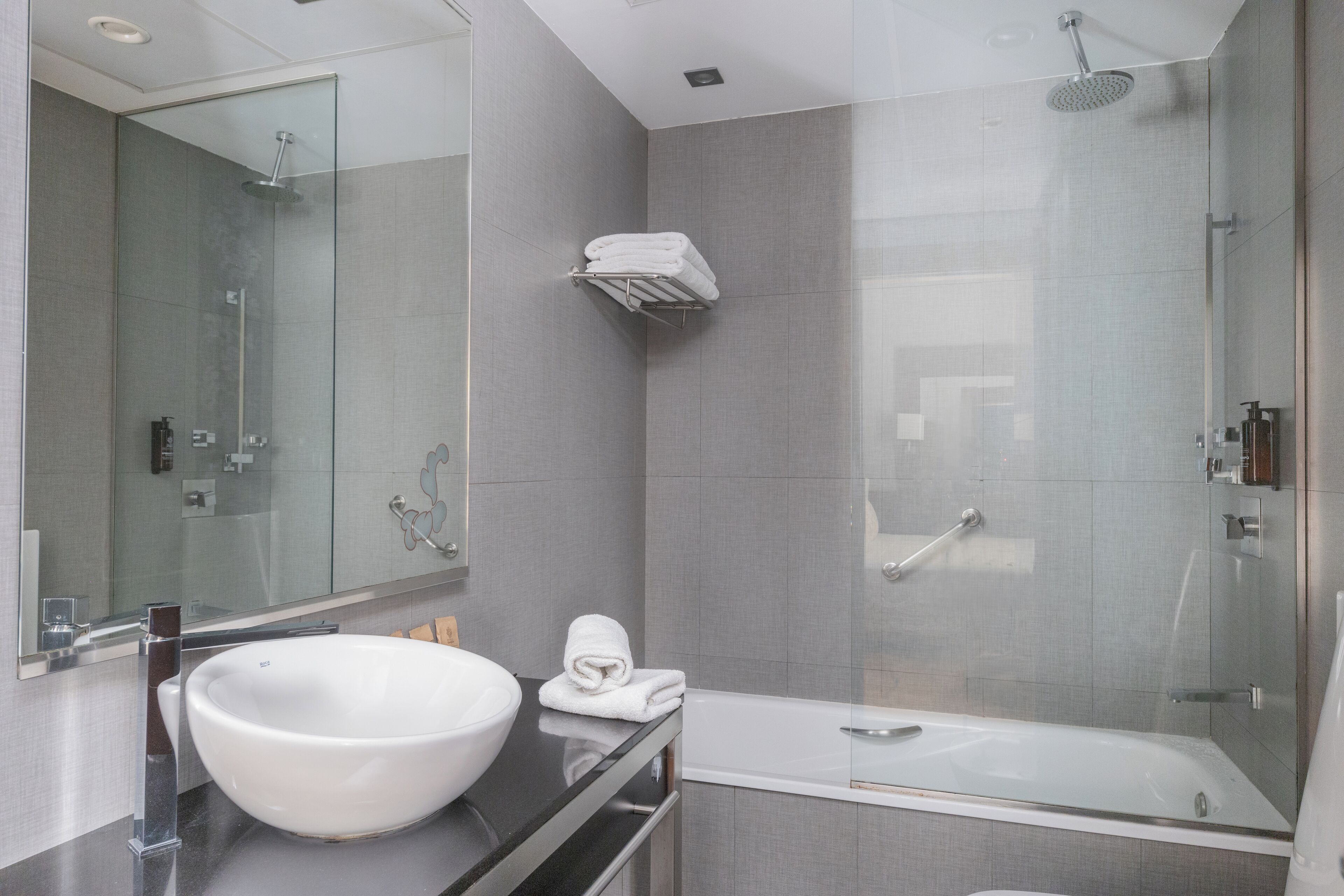 A modern bathroom with a large white sink, a mirror, a glass-enclosed shower, and a towel rack.