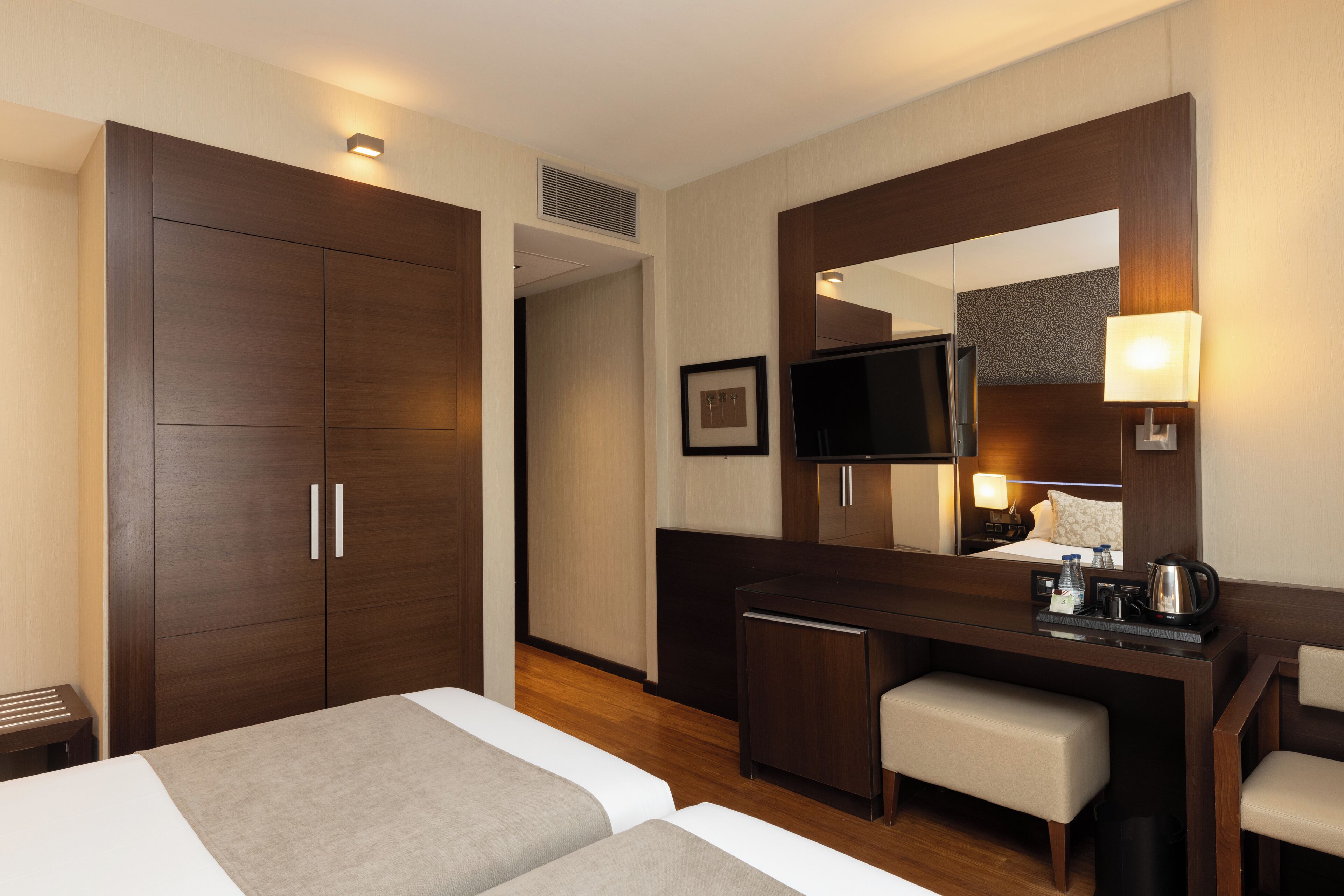 Una habitación de hotel con una cama, un escritorio con una silla, un televisor y un espejo.