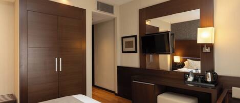 Una habitación de hotel con una cama, un escritorio con una silla, un televisor y un espejo.