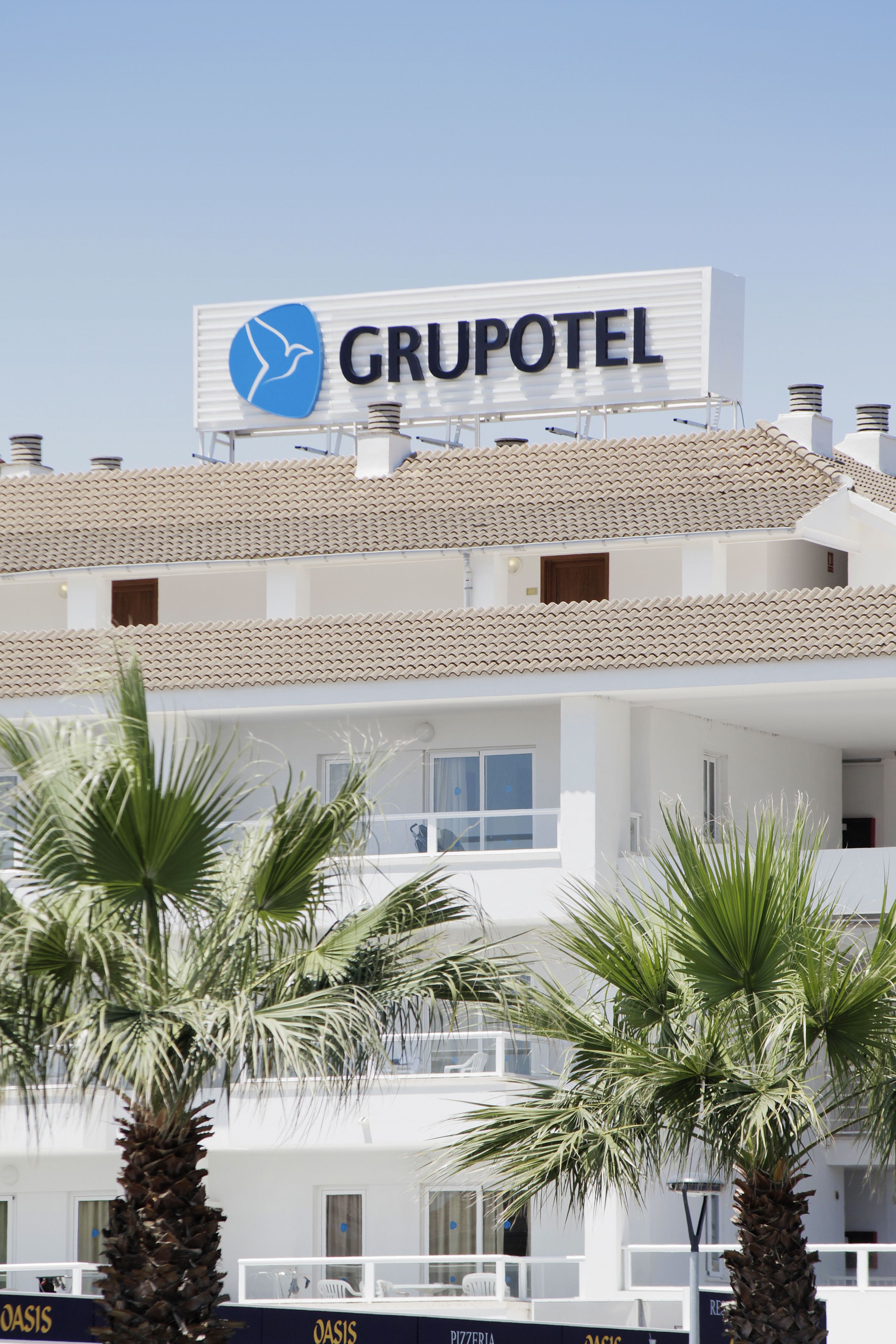Un hotel con un llamativo letrero 'GRUPOTEL', varios balcones y palmeras al frente.