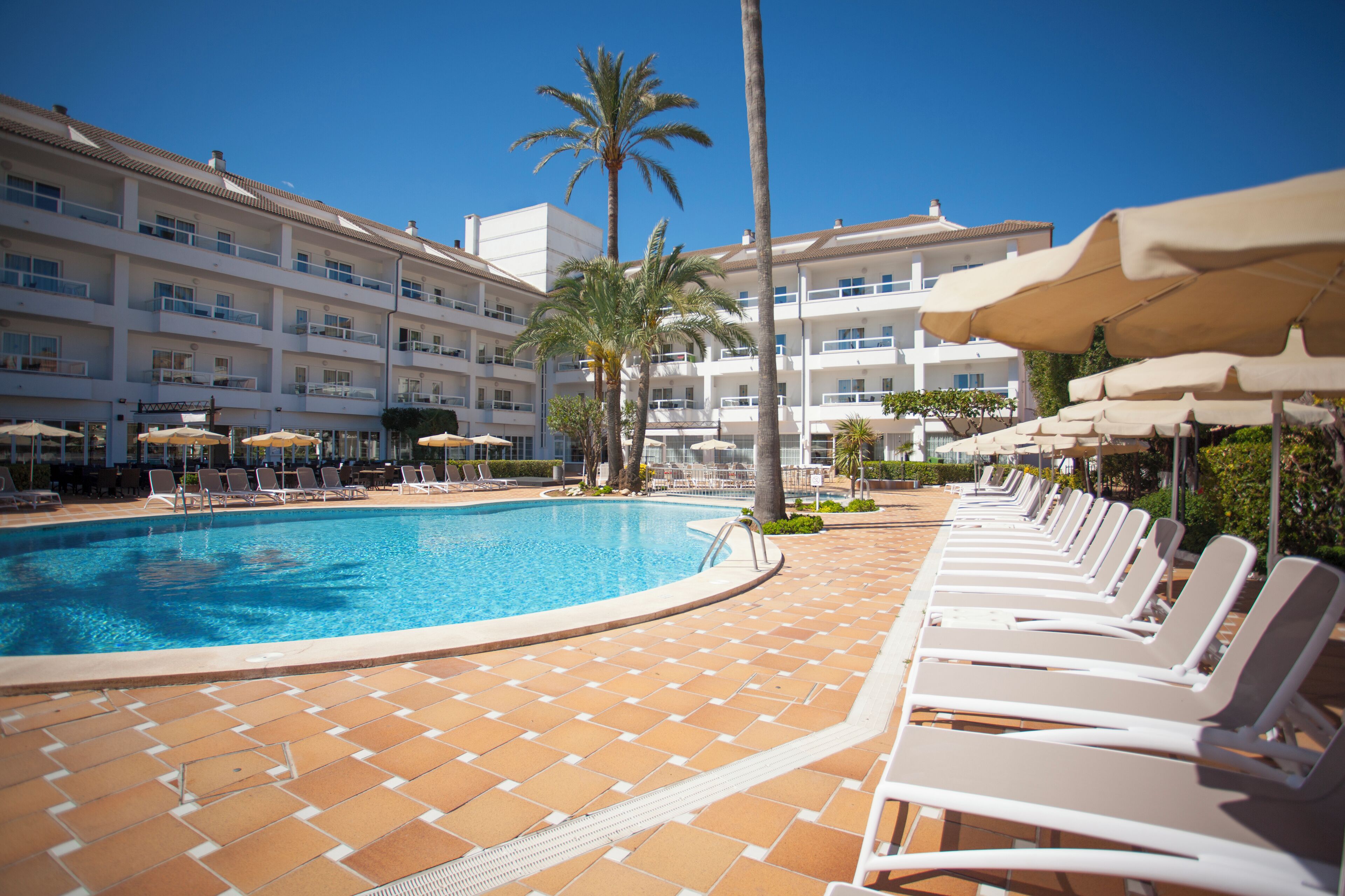 Ein Swimmingpool mit Liegestühlen und Sonnenschirmen, umgeben von einem mehrstöckigen Hotelgebäude.