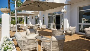Un espace extérieur aménagé avec des meubles en osier et des parasols, de grandes fenêtres et une terrasse en bois.