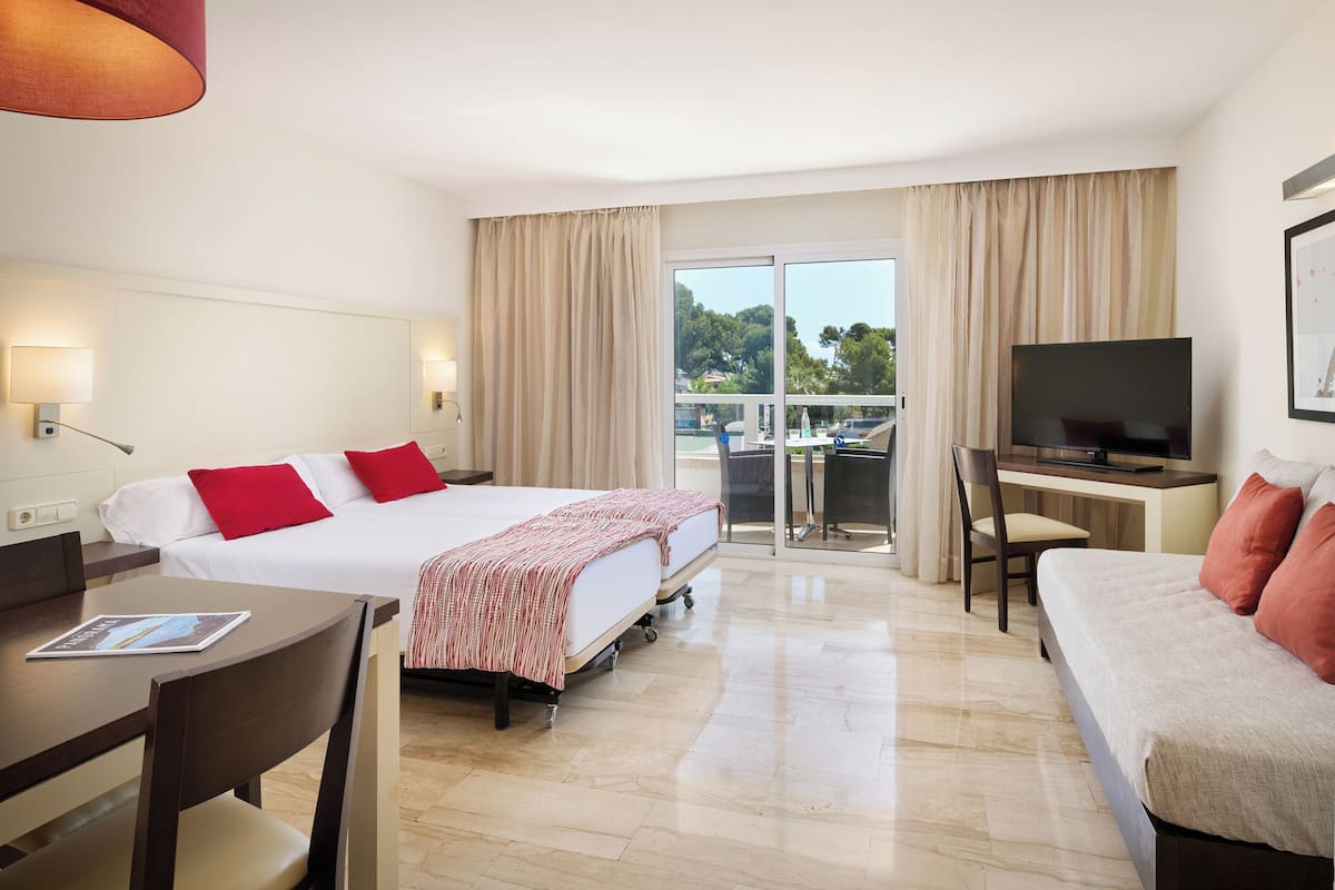 Habitación de hotel con cama, escritorio, televisor y balcón con cortinas.