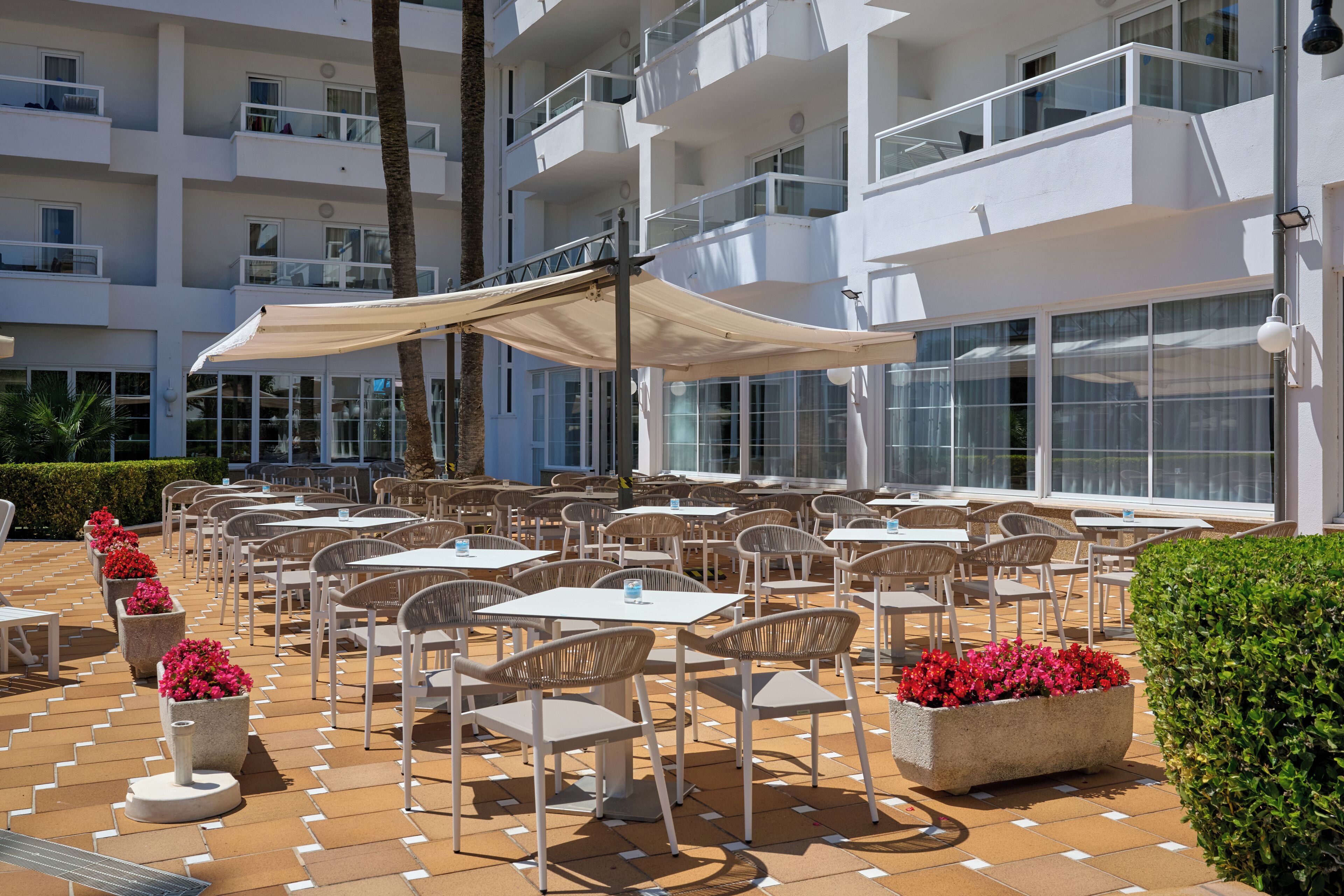 Un patio exterior con varias mesas y sillas, rodeado por un edificio blanco con balcones.