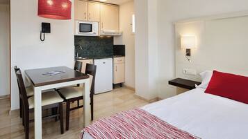 Une chambre d’hôtel compacte comprenant un lit, une petite kitchenette, un coin repas et un bureau.