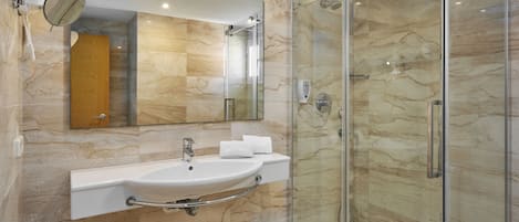 A modern bathroom with a marble wall, a glass shower enclosure, and a built-in sink with a towel rack.