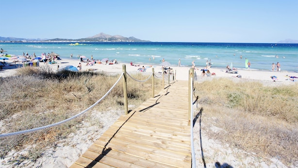 Une promenade en bois qui mène à une plage où des gens se prélassent au soleil et se baignent.