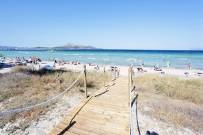 Une promenade en bois qui mène à une plage où des gens se prélassent au soleil et se baignent.