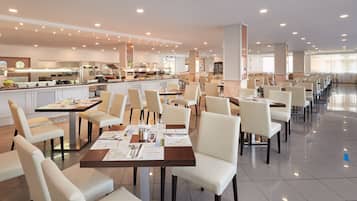 Ein geräumiger Essbereich mit mehreren Tischen und Stühlen, ein Buffet mit verschiedenen Speisen und eine moderne Küche im Hintergrund.