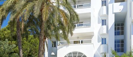 Et moderne hotel med overdækket indgang, palmer og flag.