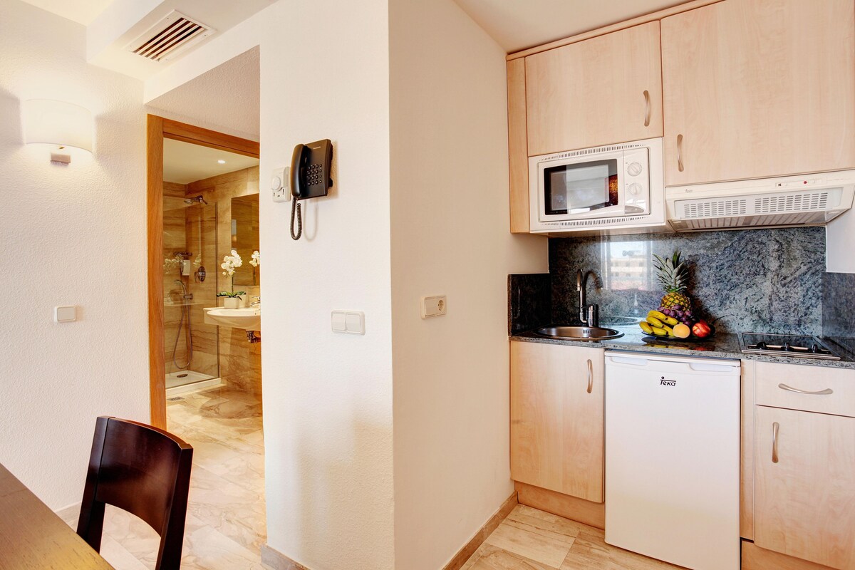 Una cocina compacta con armarios de madera, un microondas y un refrigerador pequeño.