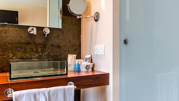 Un baño con tocador de madera, lavabo de vidrio, espejo y barra para toallas.