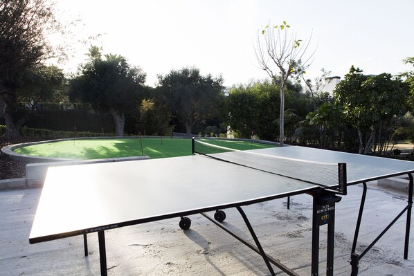 A ping pong table in an outdoor area with a green artificial turf and trees in the background. - El Plantio Golf Resort (Alicante)