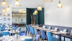 En modern restaurang med blå stolar och bord, hängande taklampor och inramade tavlor på väggen.