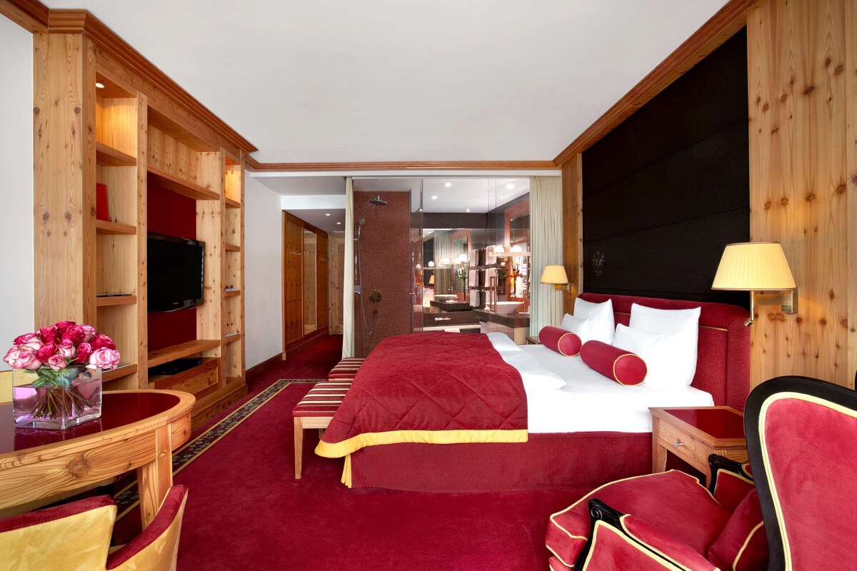 Habitación de hotel con una cama grande, paneles de madera, un televisor, un escritorio con un florero y vistas al área de la cocina.
