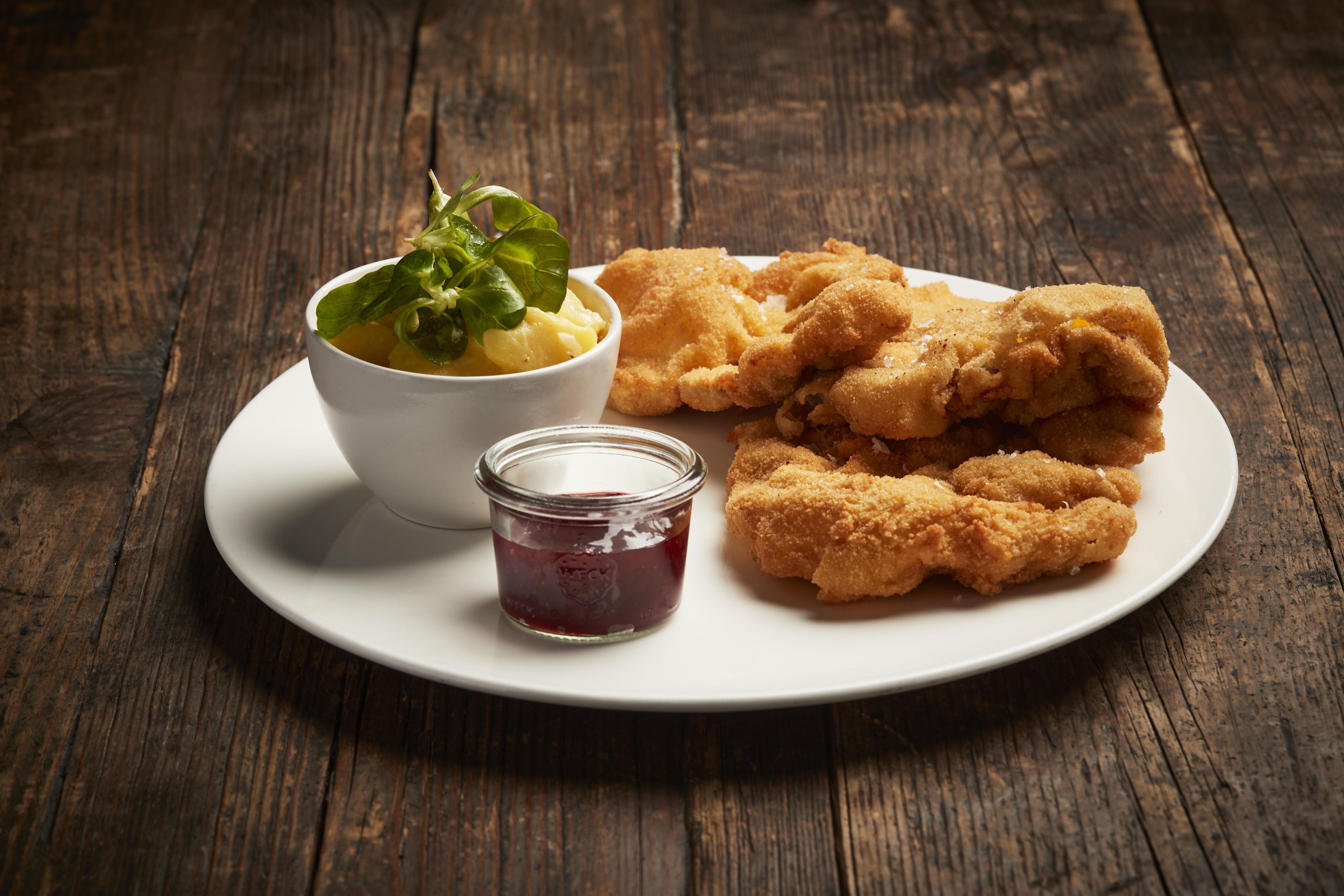 Un plato con comida frita y un bol de papas con vegetales, además de un frasco pequeño de salsa.