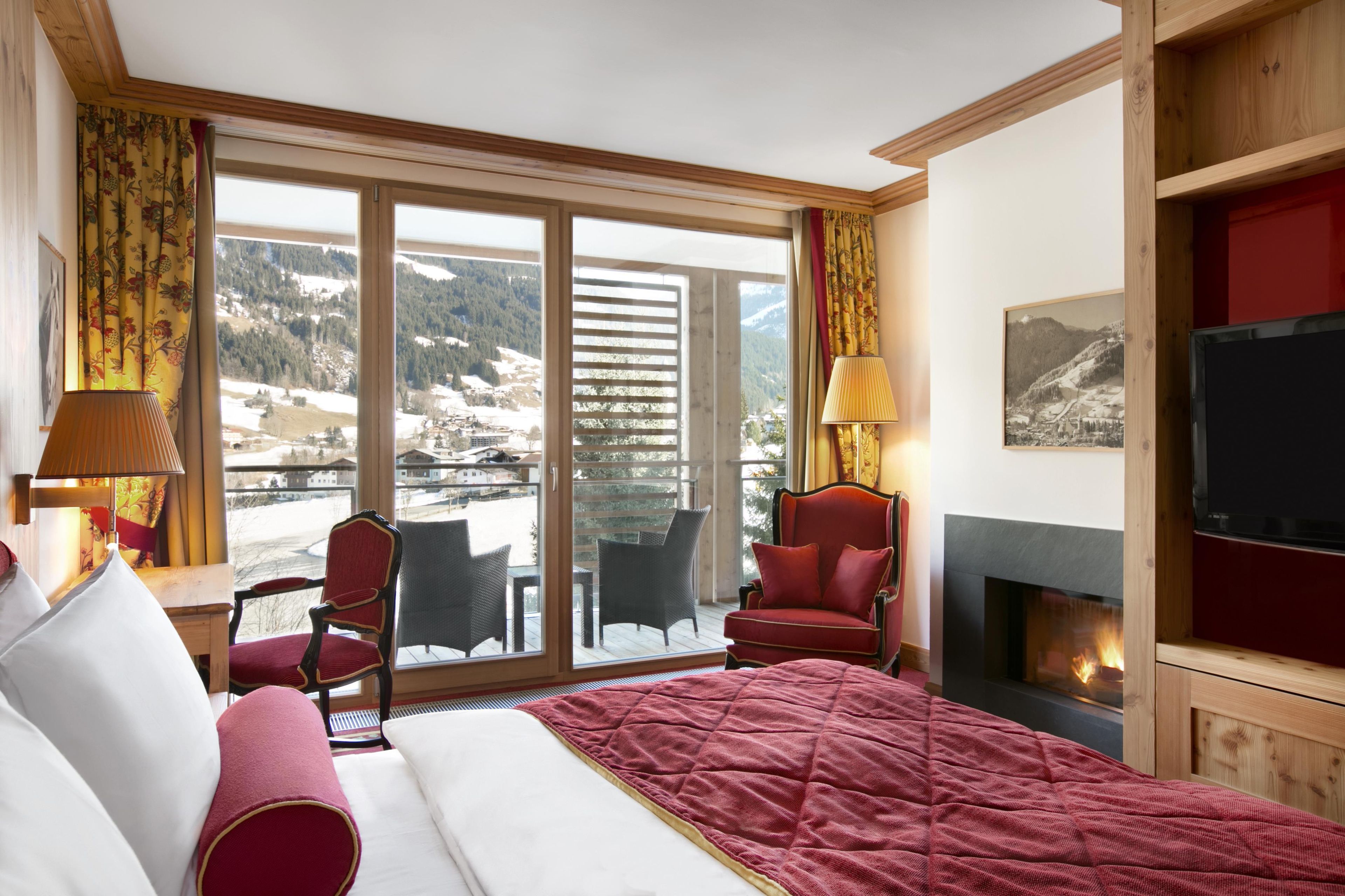 Habitación de hotel con cama, dos sillones, chimenea y un ventanal con vistas a la montaña.