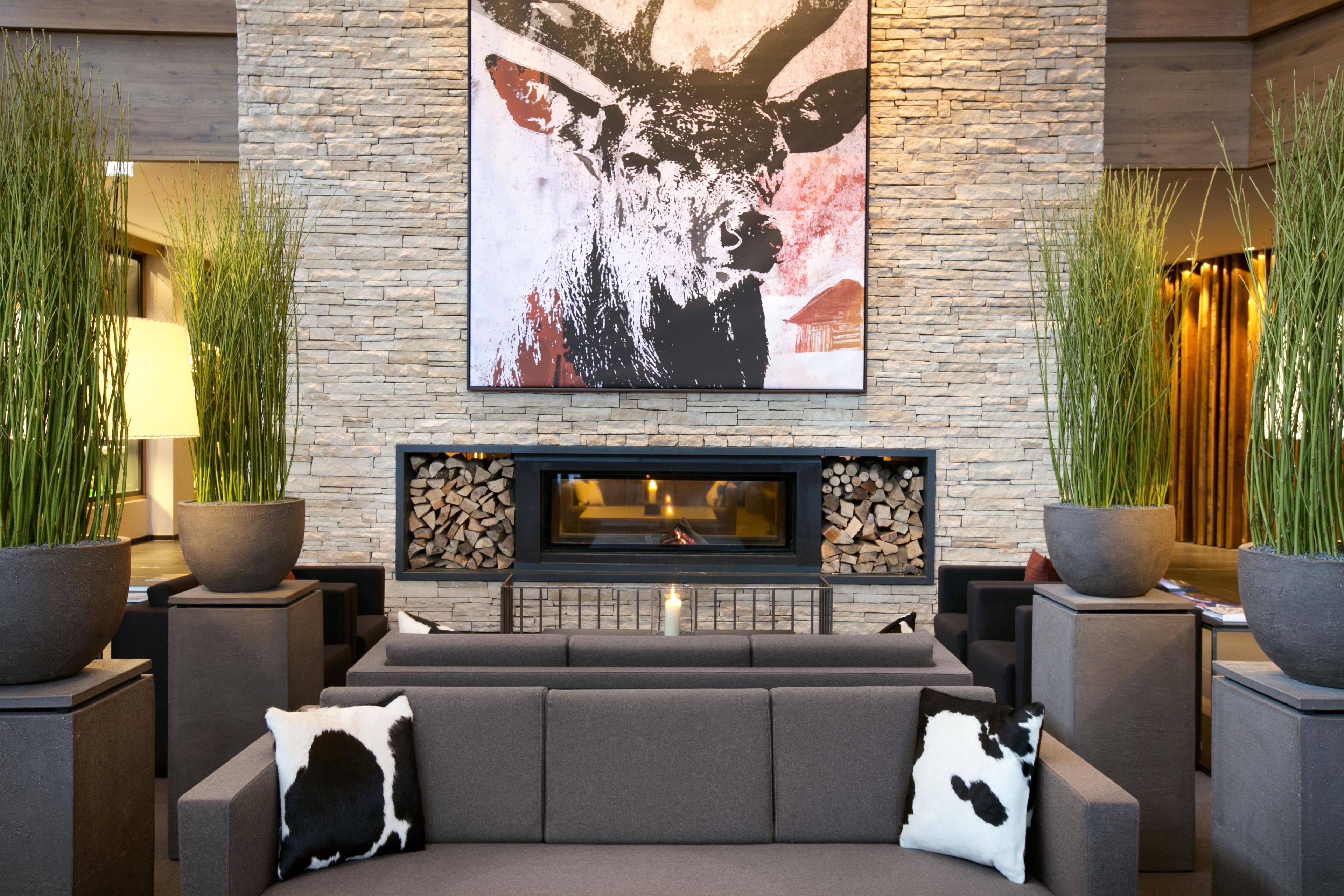 A modern living room with a stone fireplace, a large abstract painting, and two large potted plants.