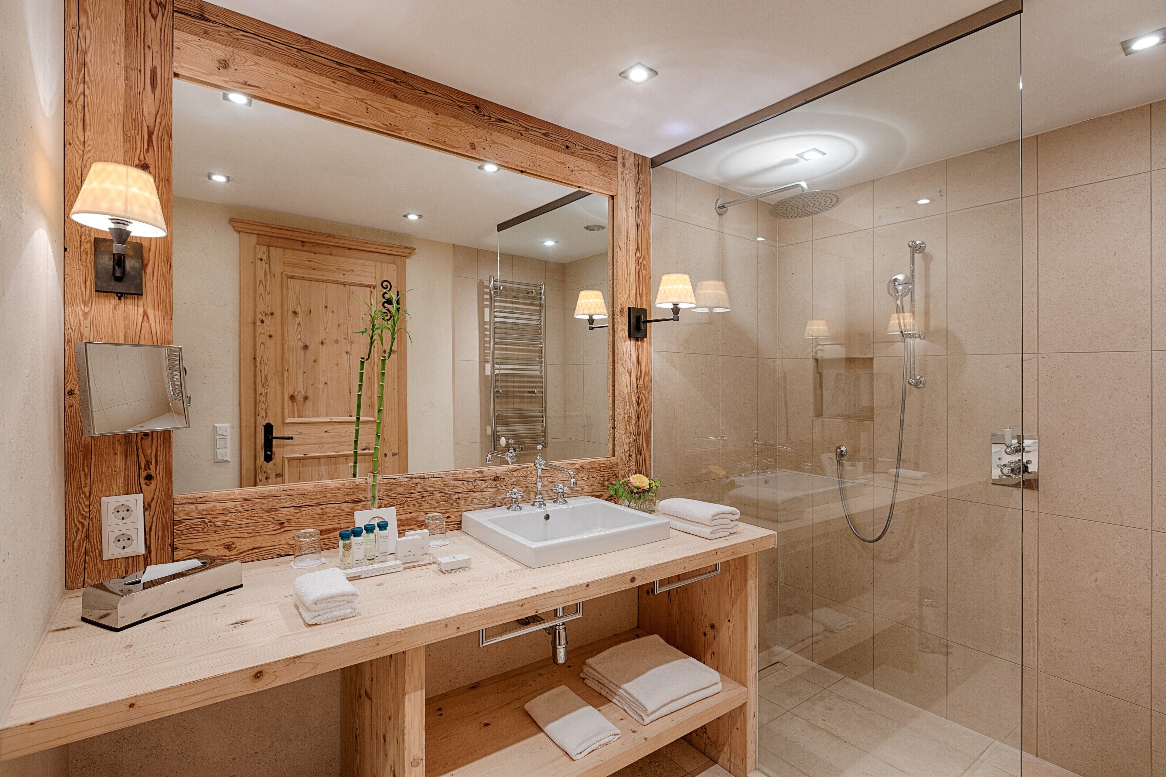 A modern bathroom with a wooden vanity, a large mirror, a shower, and a glass-enclosed shower area.