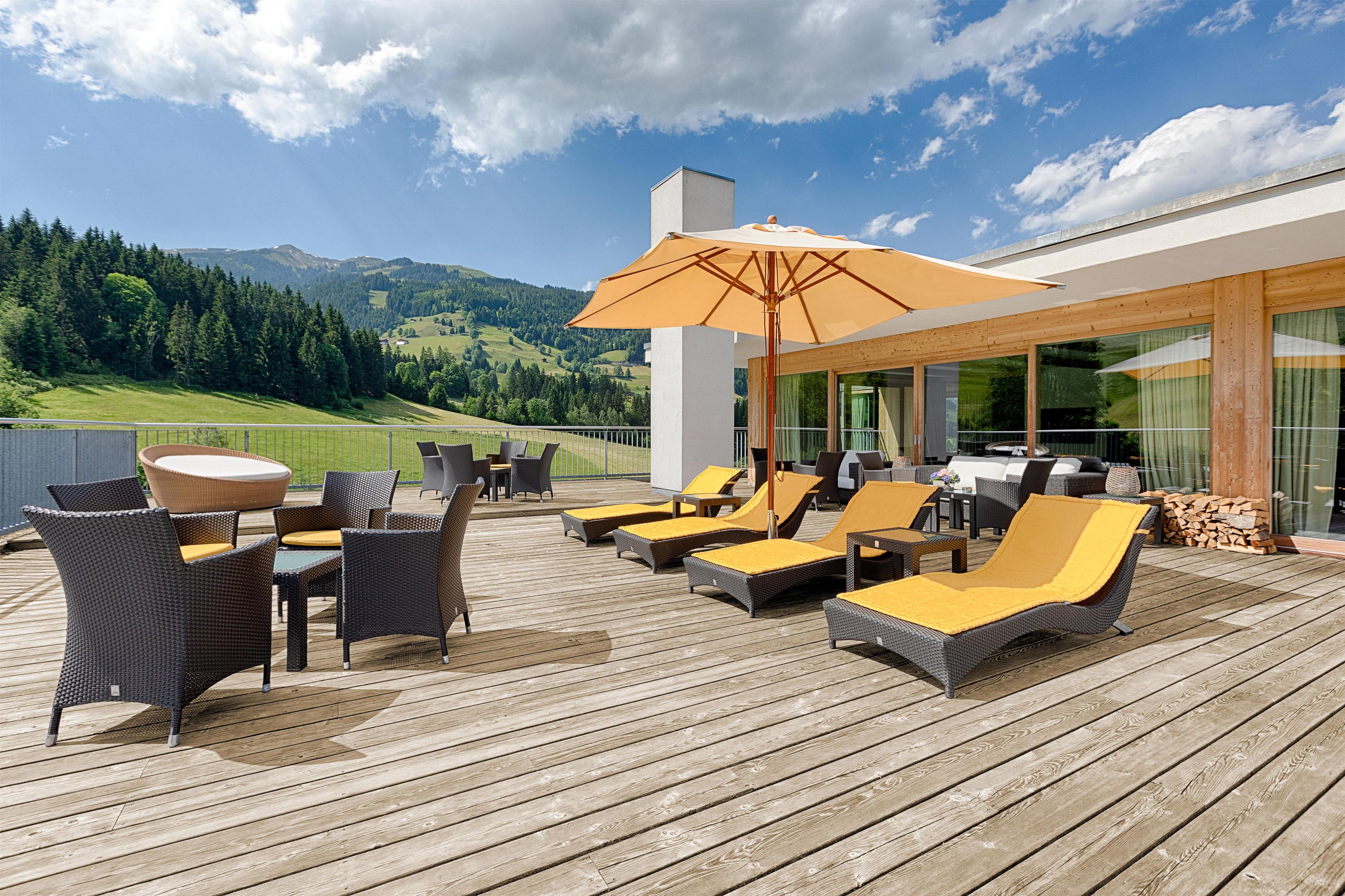 A deck with outdoor furniture, including chairs and a table, overlooking a mountainous landscape.