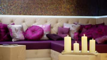 A cozy living room with a beige sofa adorned with purple and pink cushions, and three lit candles on a wooden side table.