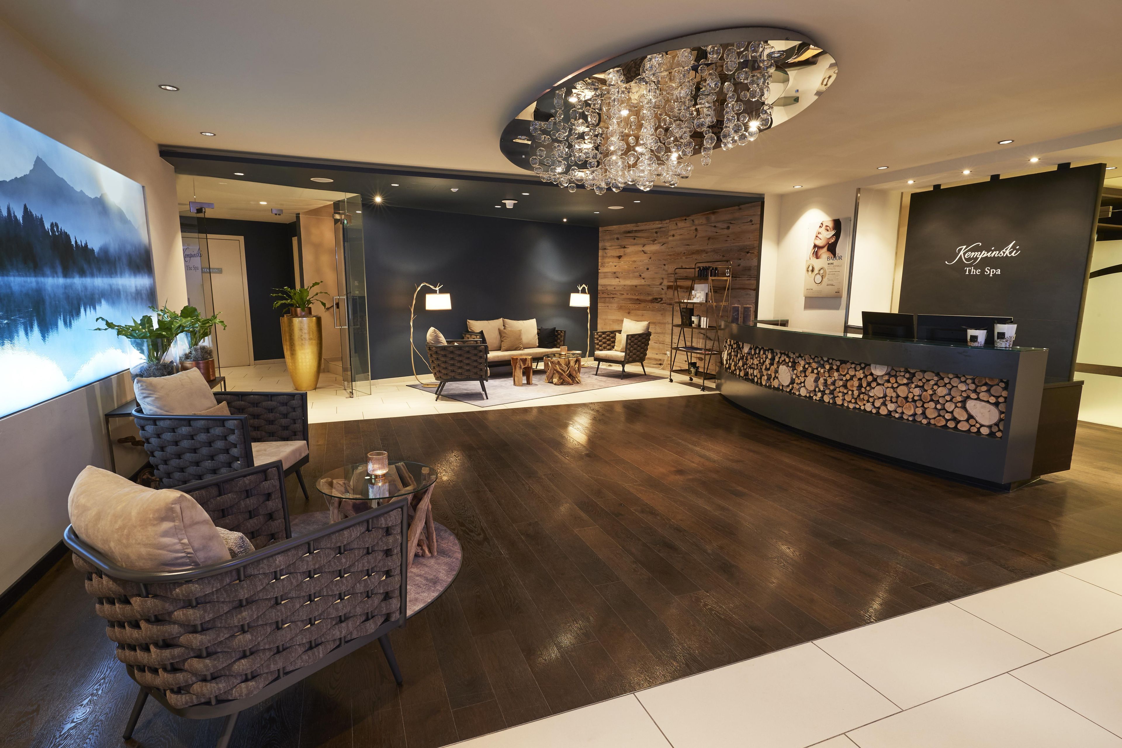 A modern reception area with a wooden reception desk, seating area with sofas and chairs, and a large chandelier.