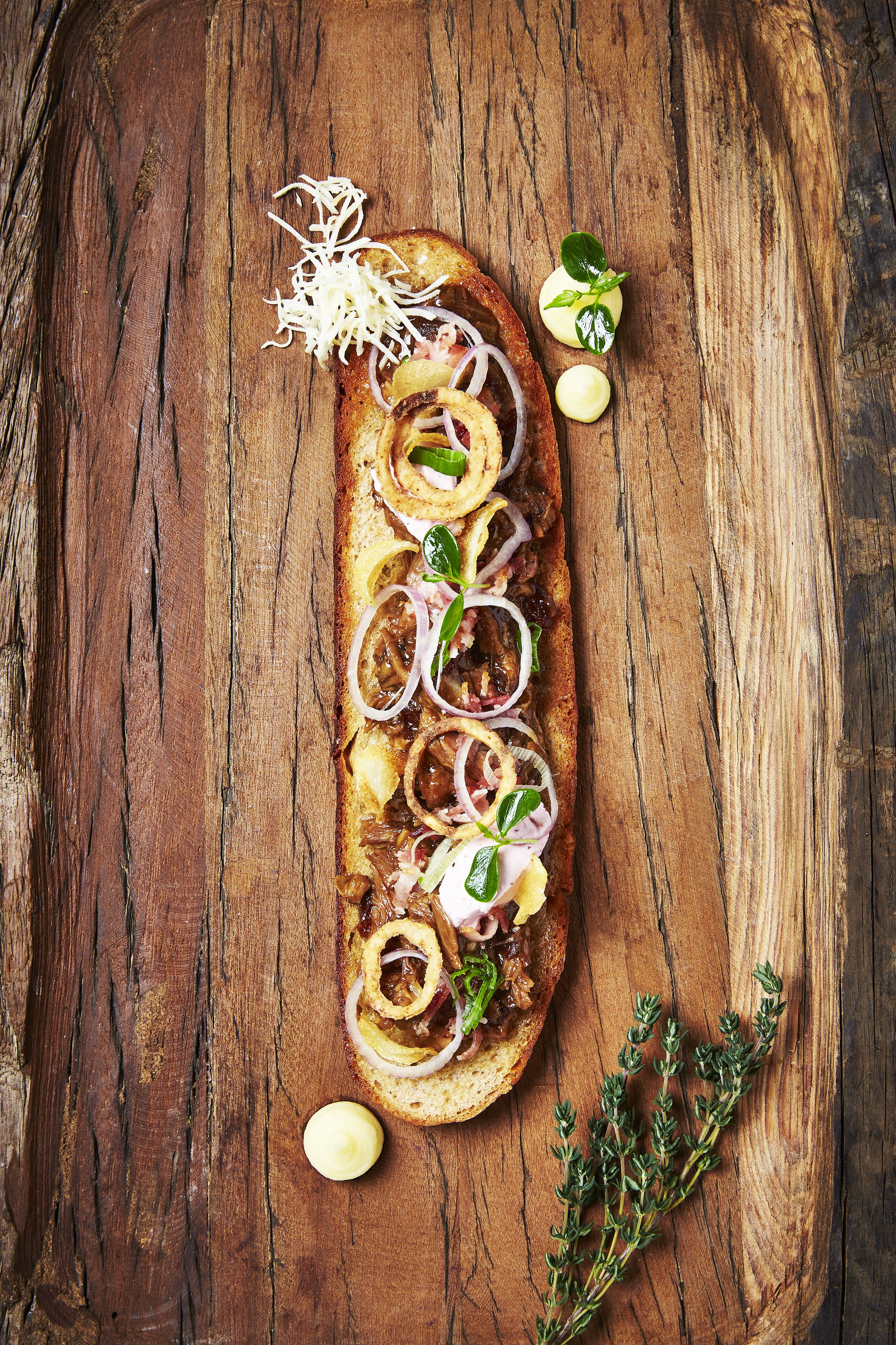 Une surface en bois sur laquelle se trouvent un sandwich et quelques herbes aromatiques.