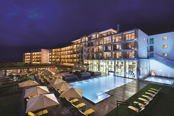 A multi-story hotel with a swimming pool and outdoor seating area. - Kempinski Hotel Das Tirol (Jochberg)