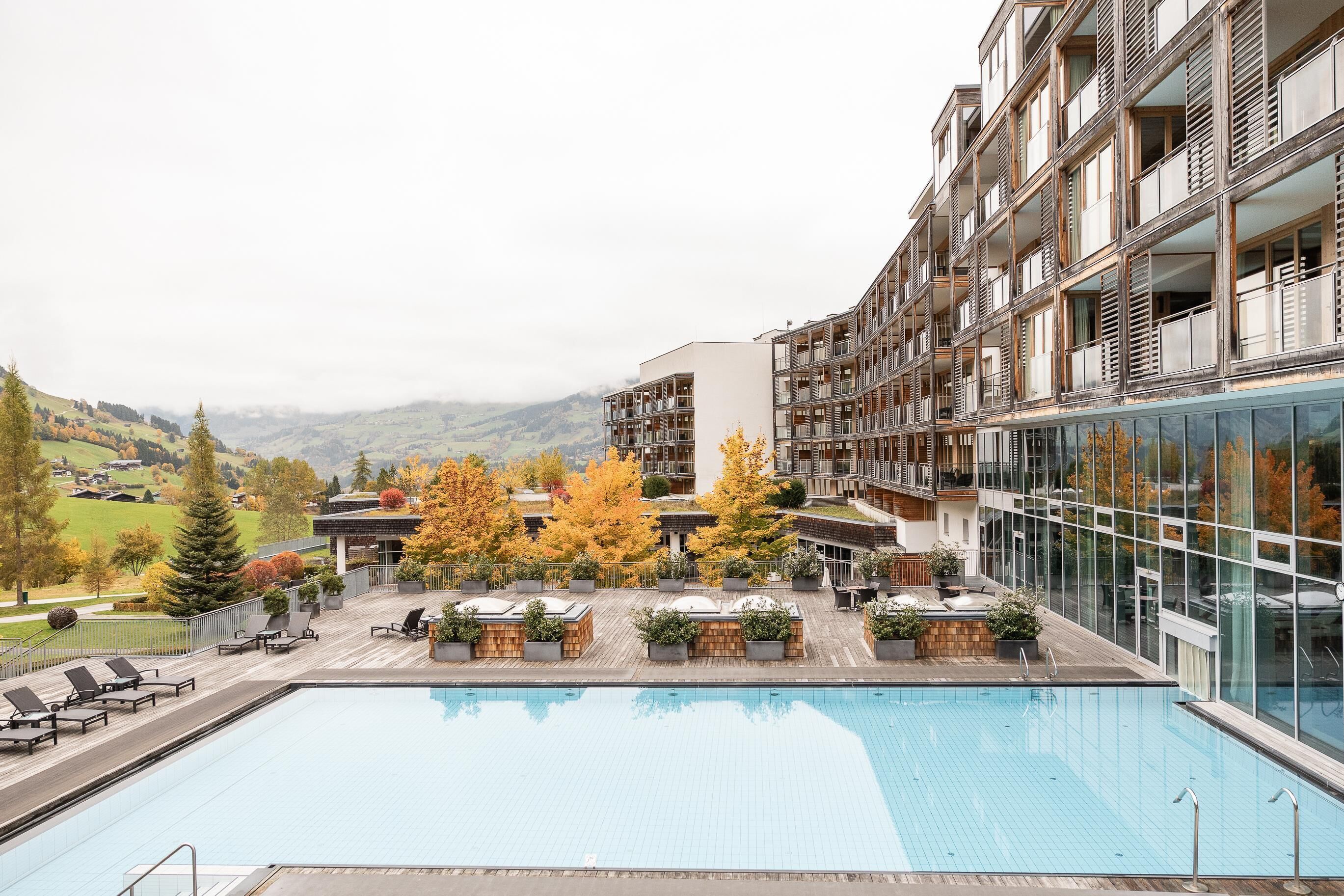 A modern hotel with a pool, outdoor seating, and a view of the surrounding hills.