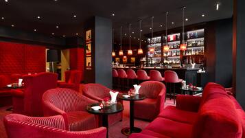 Zona de bar con sillas tapizadas en rojo, una barra y una variedad de botellas y vasos.