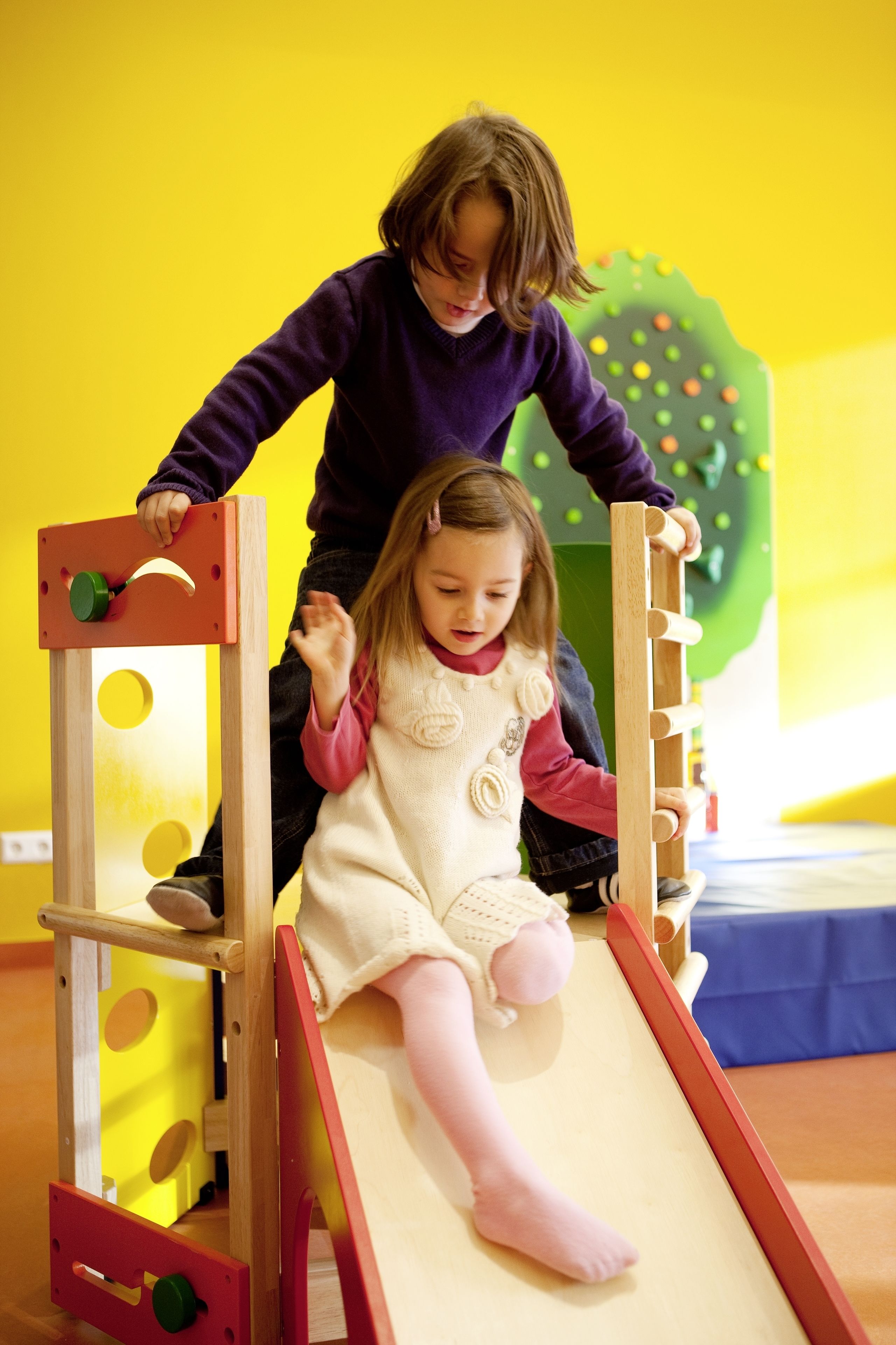 A child on a wooden slide with a yellow background.