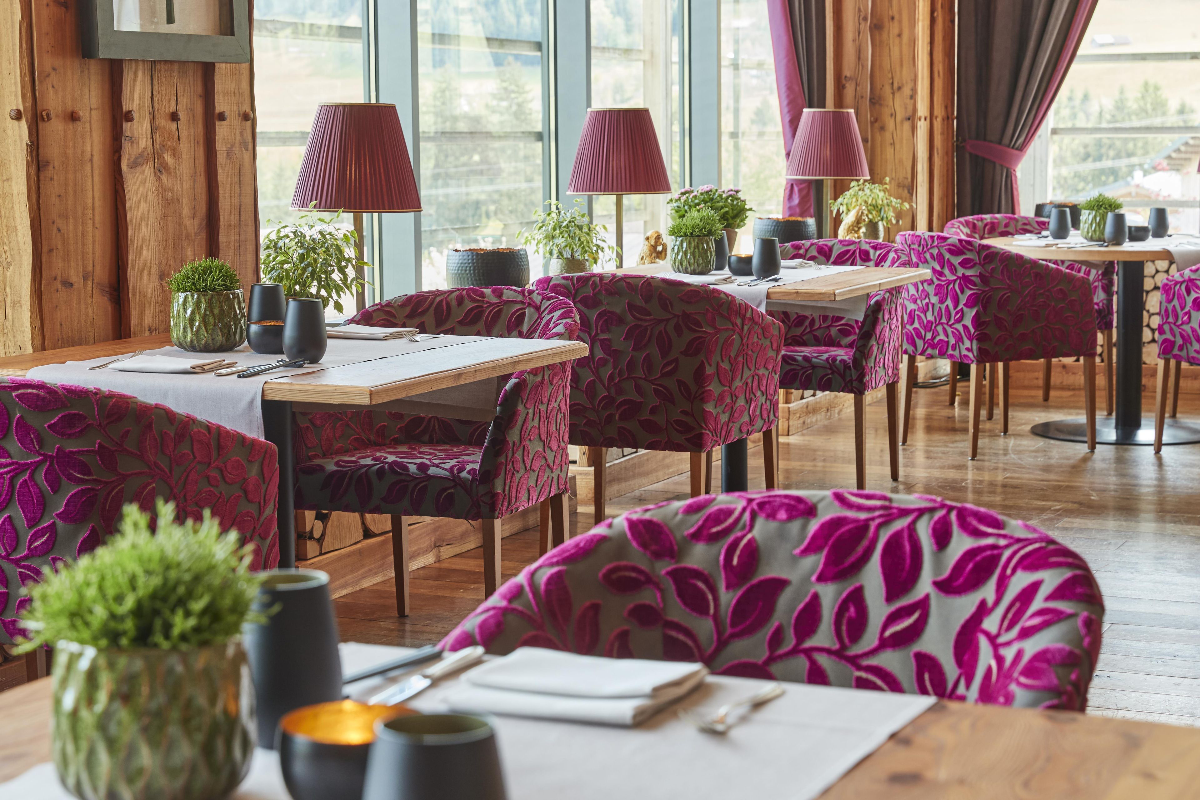 En restaurantindretning med trævægge, borde med stole betrukket med lilla blade, og plantet blomster.
